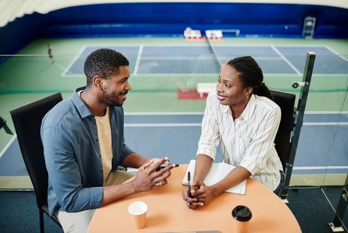 Two coaches talking at table in tennis arena.