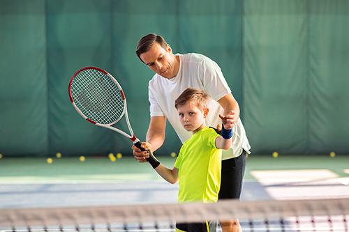 Coach assisting young tennis athlete.