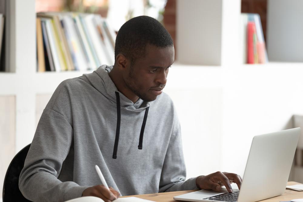 Teen male on laptop and writing on paper.