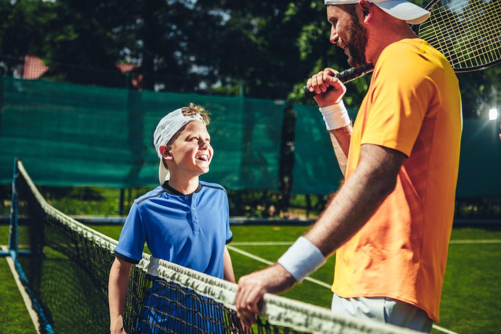 Tennis coach and young athlete talking and smiling.