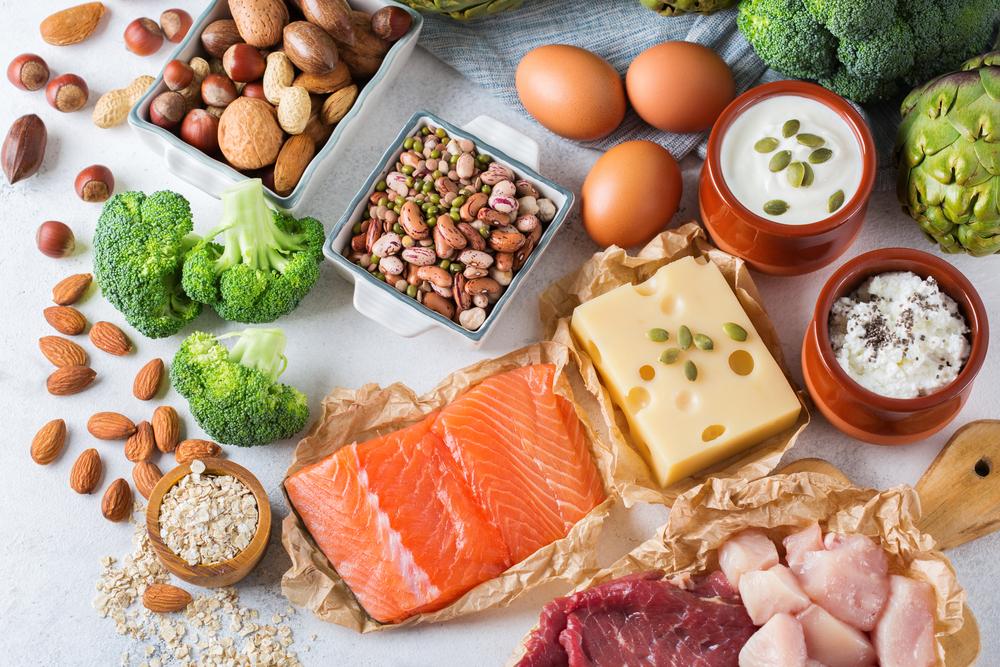 Various foods full of protein including fish, cheese, nuts, and broccoli.