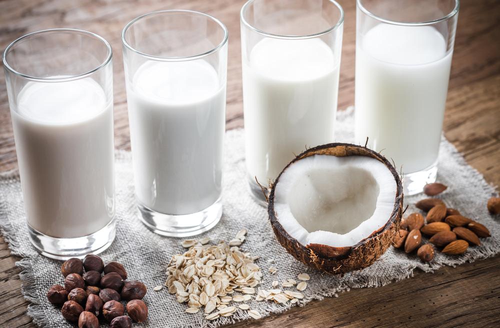 Glasses of milk next to the source, including coconut, almond, and oat.