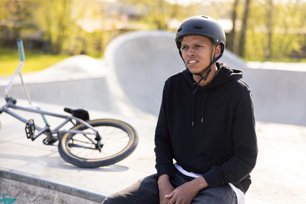 Male teen wearing helmet in skate park next to BMX bike.