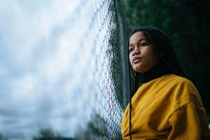 Teenage girl looking into distance next to fence.