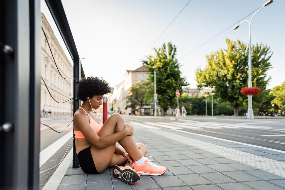 Teen girl athlete sitting outside against wall looking down.