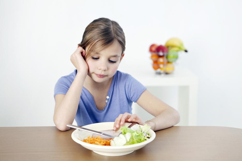 Young girl looking sadly at plate of food.