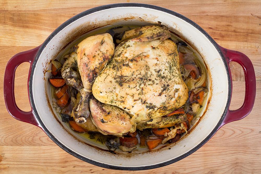 A whole chicken with vegetables fully cooked in a crock pot.