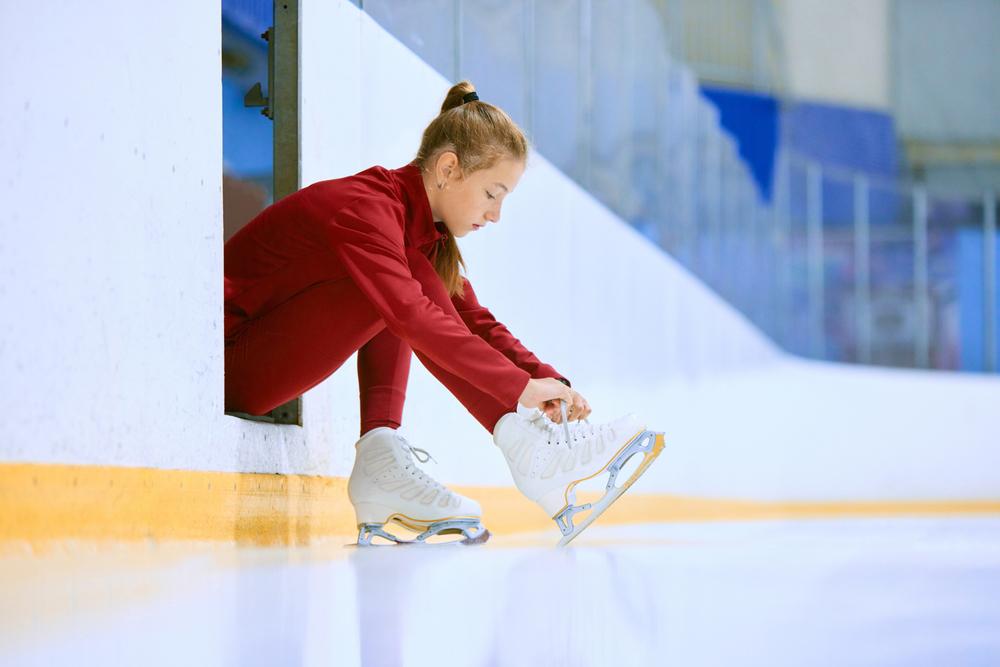 Female figure skater lacing up skates on edge of ice rink.