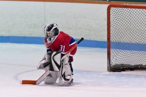 Young kid hockey goalie alone in front of goal on ice.