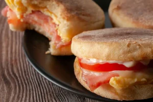 Close up of an english muffin with egg, meat, cheese and tomato.