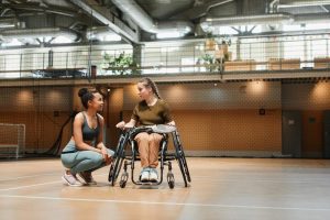 Coach talking to wheelchair badminton athlete on court.