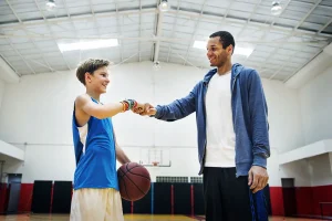 Coach fistbumping young basketball player on court.