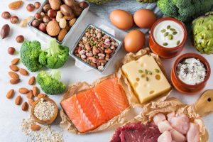 Various foods full of protein including fish, cheese, nuts, and broccoli.