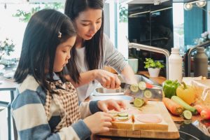 Mom helping prep sandwiches with young daughter.