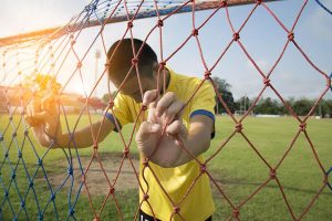 Young asian boy holding soccer goal net looking down.