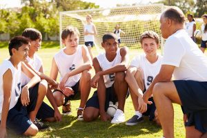 Male coach talking to diverse group of male teen soccer players.