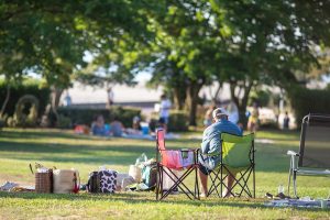 Parent sitting on sidelines outside with coolers and bags.