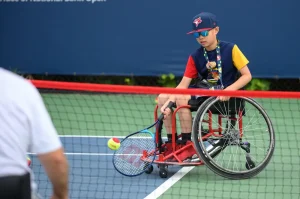 Young mane in a wheelchair playing tennis.