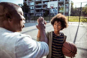 Young man high fiving his grandfather on a basketball court.