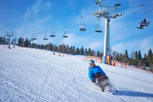 Young man on seated skiis goin down a snowy mountain with a chairlift in the background.