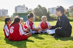 Coach sitting with a youth girl's soccer team talking.