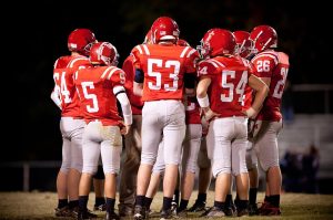 Football team huddled on field during night game.