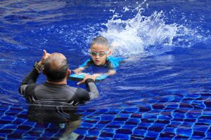 Young boy being coached with a kickboard in a pool.