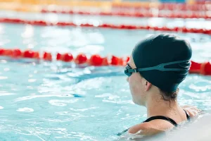 Young woman with a swimming cap and goggles in a pool lane.