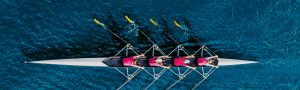 rowers rowing together in boat on blue water