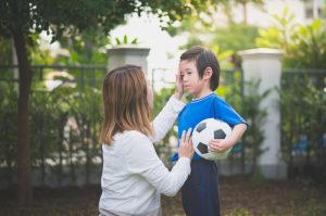 Mother kneeling to comfort young son holding soccer ball.