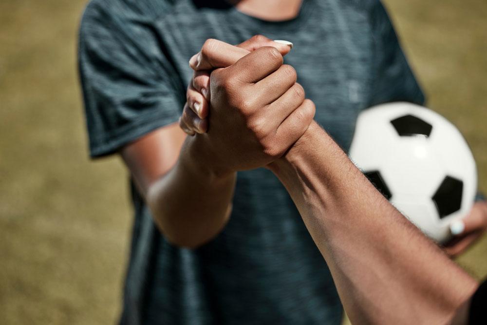 Cloes up of two young men shaking hands while one holds a soccer ball.