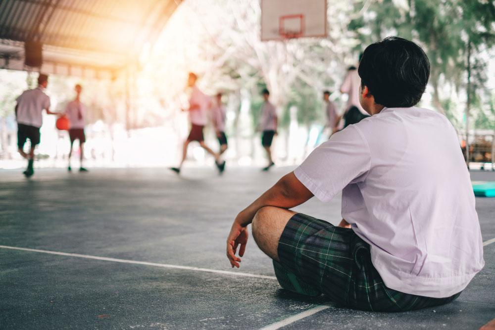 Young boy sitting on sidelines alone during basketball game.