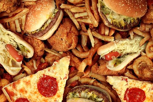 Close up of unwrapped fast food items including pizza, burgers, and fries.