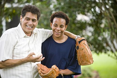 Interracial father and son holding baseball mitts.