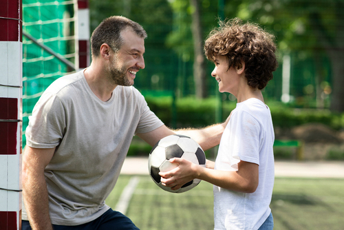 Father and son smiling and talking holding soccer ball.