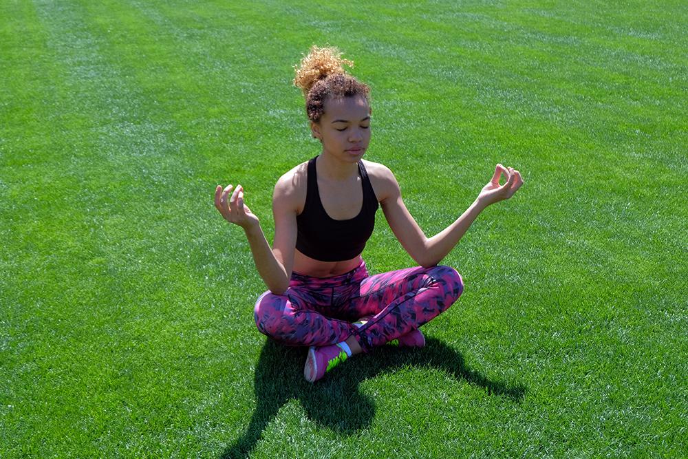 Young woman meditating outside on grass.