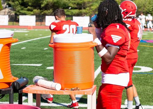 Football player on sideline next to water cooler.