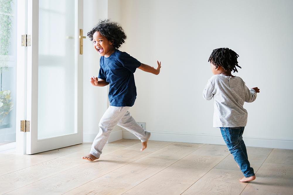 Two young black children running barefoot indoors with smiles.