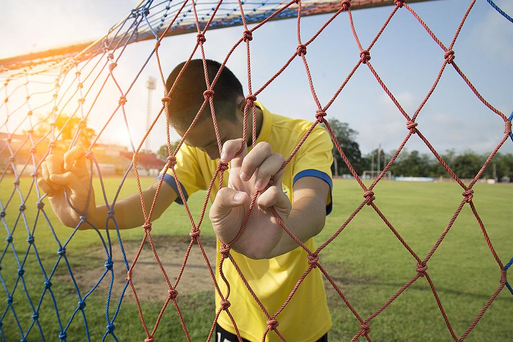 Young asian boy holding soccer goal net looking down.