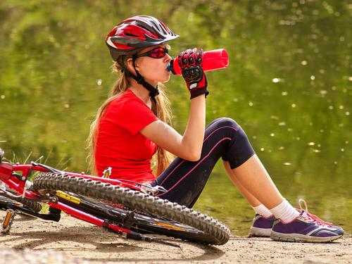 Teen girl drinking water with helmet on next to bike.