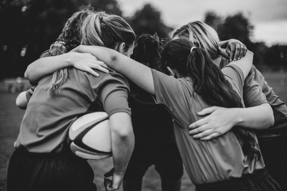 Girls rugby team huddle in black and white.