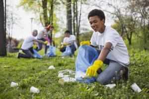 coping with quarantine Young boy picking up trash with friends wearing gloves.