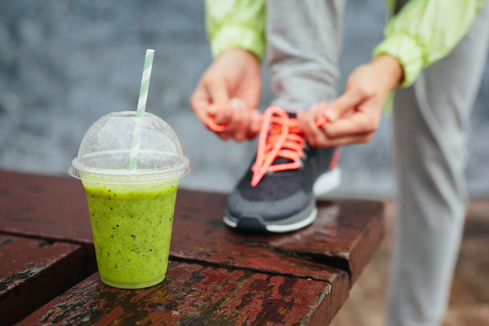 Close up of a green smoothie with someone tying a gym shoe behind it.