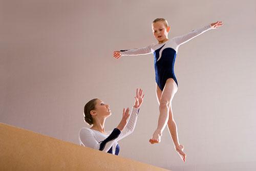 Young female gymnast on balance beam with coach.