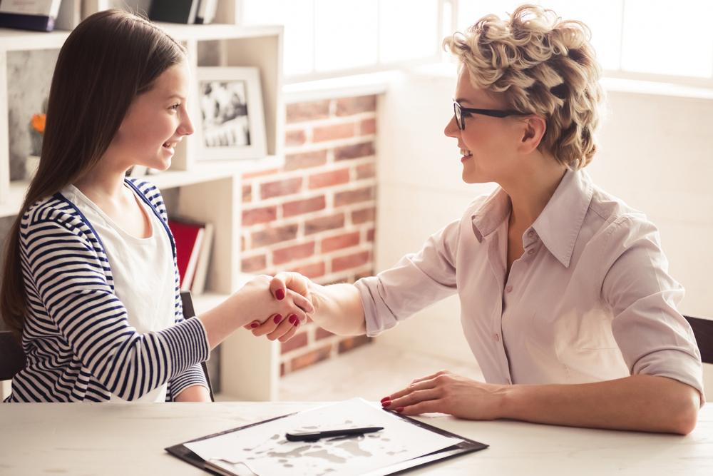 Girl shaking hands with adult in office setting.