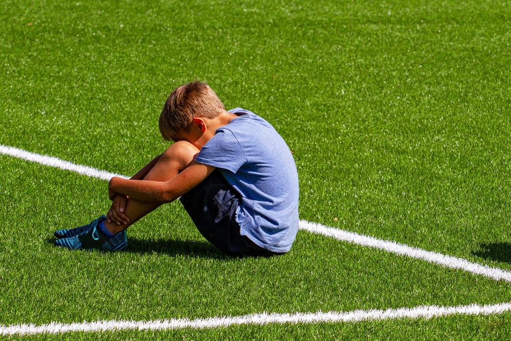 Young white boy sitting on soccer field with head on news.