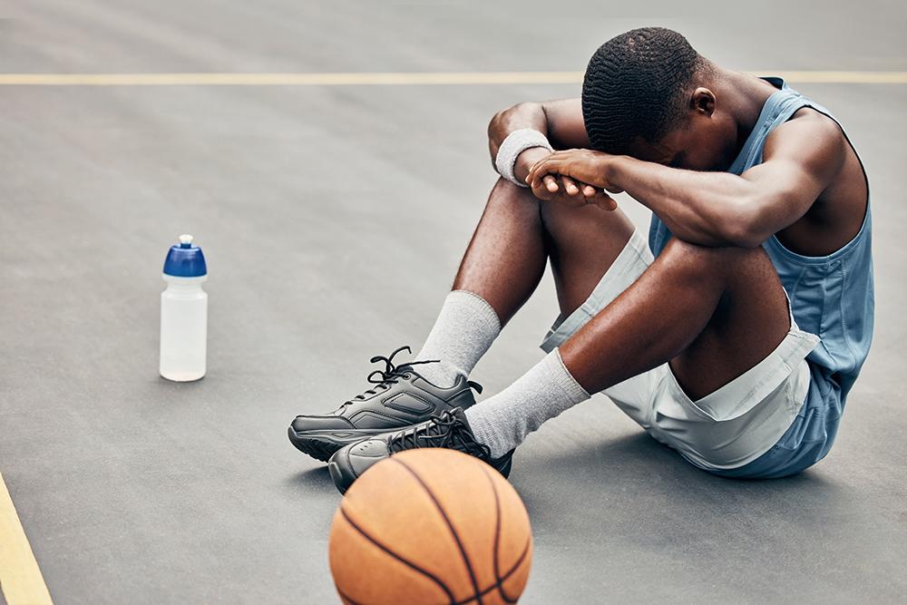 Young male basketball player sitting on ground with head on arms.