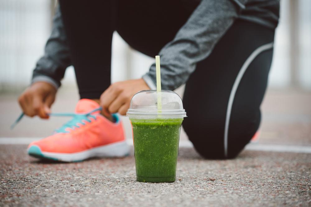 Woman tying shoes behind a green smoothie.