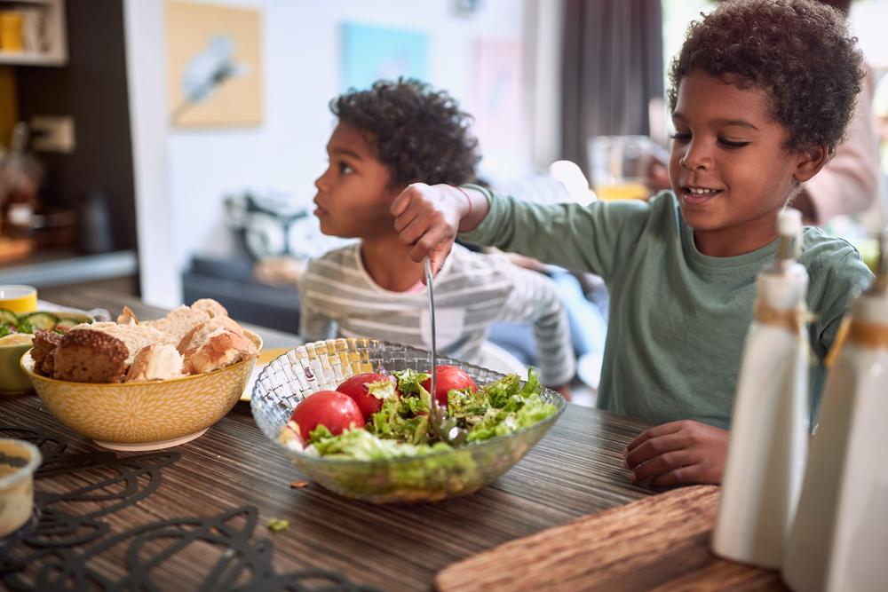 Young boys eating salad and bread at table.