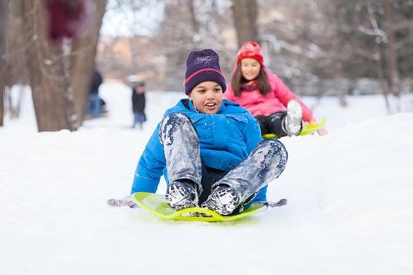 Young boy and girl sledding down a snow covered hill.
